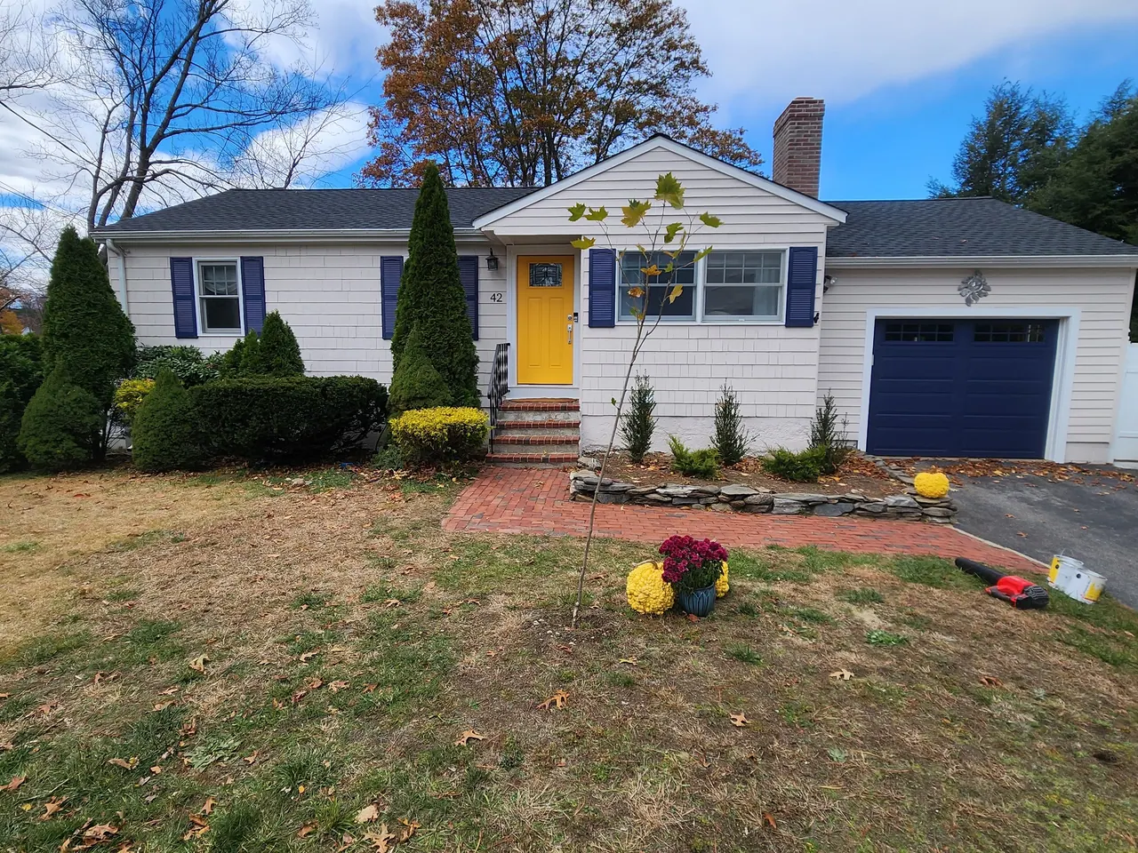After: the same ranch painted white with navy shutters, a navy garage door and a yellow front door