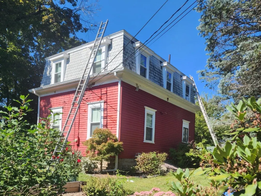 Before: mansard-roof house with faded red siding, ladders up against the wall, garden in front